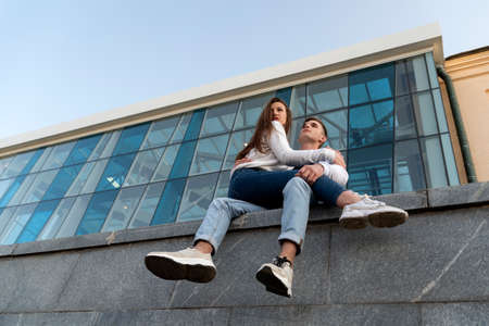Date of a young couple. Girl is sitting on the lap of the guy. Modern city building on the...