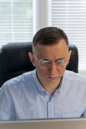Young man with glasses is working on a project. Portrait of a man while working at a computer. Young man is working on the projectの写真素材