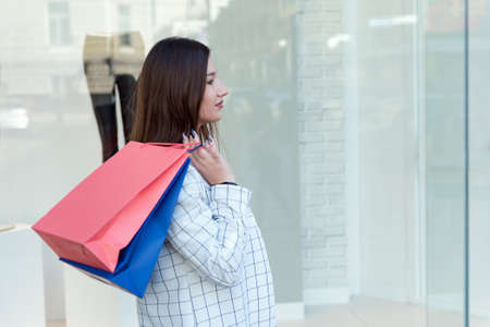 Tired brunette holding shopping bags on showcase background. Black Friday. Exhausting shopping.の写真素材