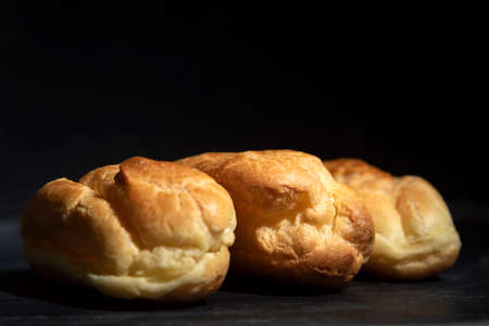 Profiteroles, puffs, popovers, eclaires on black background close up