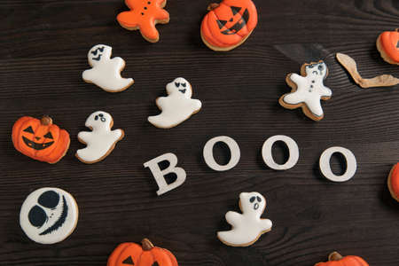 Halloween decor of orange and white cookies in the form of pumpkin, smiley, ghost, placed on a brown wooden table. Inscription Booo.の写真素材