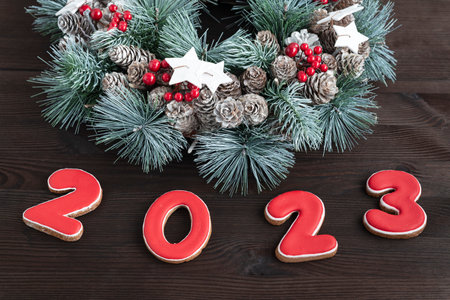 Christmas wreath and Inscription 2023 gingerbread cookie. Wooden background. Close up.