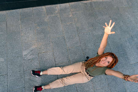 Beautiful woman with red dreadlocks enjoys life sitting on the street sidewalk. Cheerful girl on the street. Summer timeの写真素材