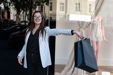 Happy young woman with black shopping bag on shop window background. Girl student after shopping...