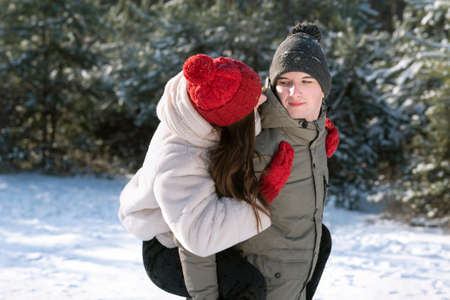 Guy carries his girlfriend on his back. Young couple having fun on frosty sunny day. Winter forest.の写真素材