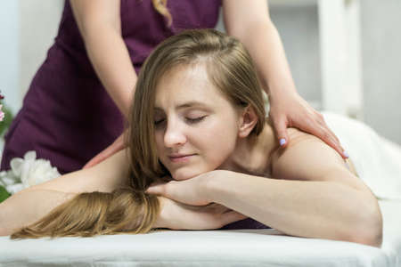 Beautiful happy woman lies in spa salon and enjoys professional massage. Pleasant environment in beauty salonの写真素材