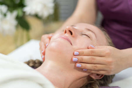 Hands of the masseur make modeling facial massage to young woman. Relaxing in the spa salon. SIde view.の写真素材