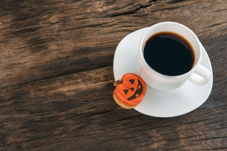 Cup of black coffee and a Halloween cookie stands on a brown wooden table. Halloween food concept. Copy spaceの写真素材