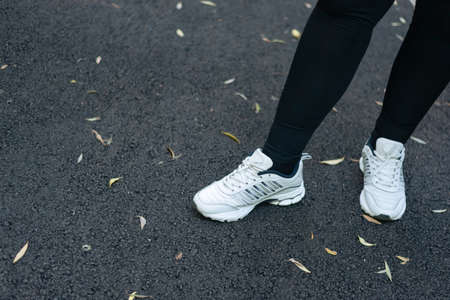 Womens feet in sports sneakers against the background of asphalt with autumn leaves. Outdoor sports.の写真素材