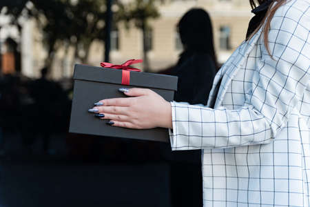 Female hands with black gift box with red bow. Woman takes a gift. Close up, side viewの写真素材