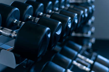 Close up black dumbbells for strength training. Equipment for sports. Different dumbbells on the rackの写真素材