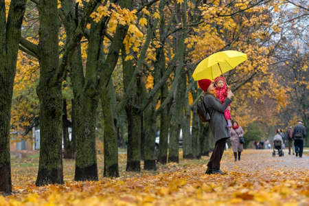 Mother holds small child and large yellow umbrella in her arms. Walk in the autumn park.の写真素材
