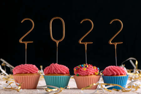 Holiday cupcake with pink glaze and 2022 numbers on black background. New year and christmas