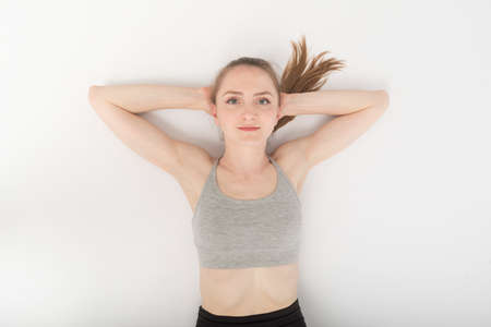 Portrait of beautiful smiling young woman in a sports top on the floor after training. Top view. Slim sports girl on white backgroundの写真素材
