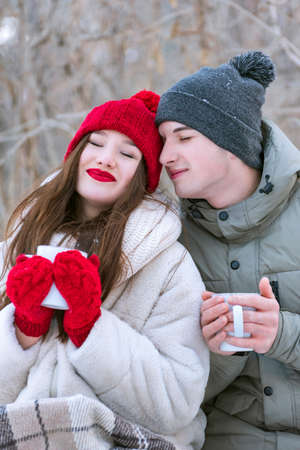 Young loving couple in winter outdoors. Girl in red hat and mittens holds mug