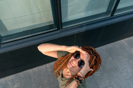 Beautiful girl with red dreadlocks in black glasses looks up at the sky and smiles. Shooting on the...