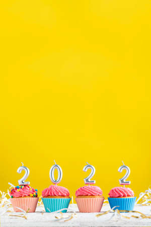 Bright Christmas theme with candles in the shape of numbers 2022 on cupcakes on yellow background. Copy spaceの写真素材