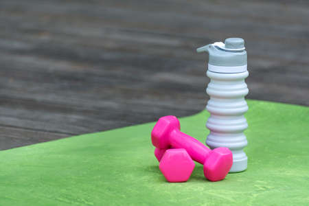 Pink dumbbells and silicone water bottle on yoga mat. Close up. Equipment for sportsの写真素材