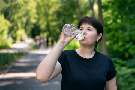 Young woman drinks water while jogging in the park. Drinking regime during sports