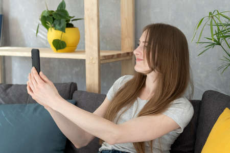 Beautiful young woman makes photo on phone. Girl takes pictures of herself on smartphone, sitting on...