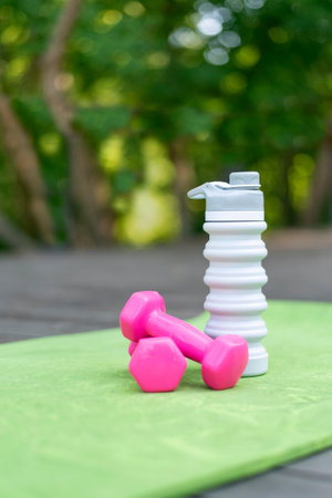 Pair of pink dumbbells and silicone water bottle on yoga mat. Fitness and activity outdoors. Sport and healthy lifestyle concept. Vertical frame.の写真素材