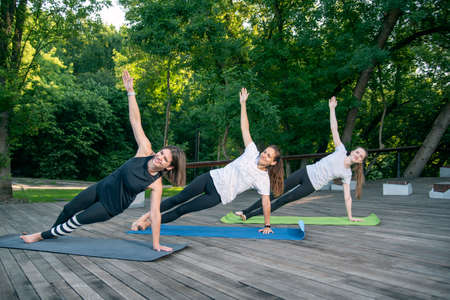 Group of happy smiling young women practice yoga early in the morning outdoors. Side Plank....
