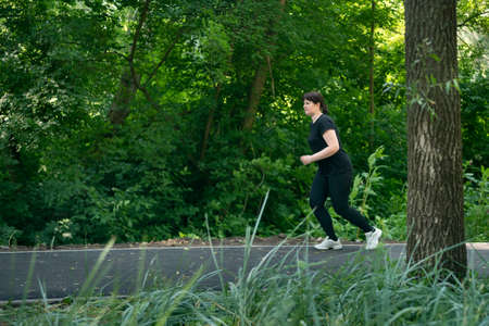 Young woman in activewear choosing healthy lifestyle. Girl runs in the park. Going to lose extra...