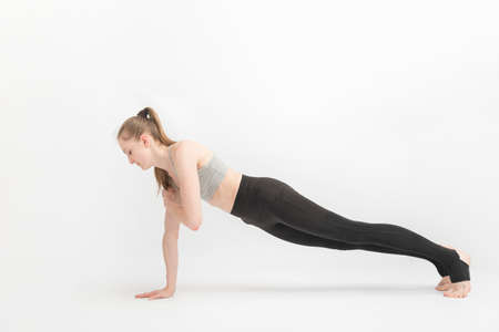 Exercise plank. Young slender woman practices yoga on white background. Fitness trainer. Yoga class
