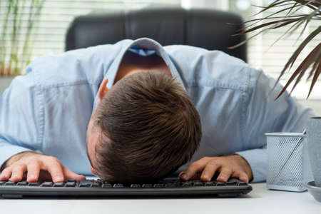 Young businessman working at computer, falling asleep in office on keyboard. Tired and fatigued...