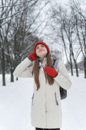 Beautiful young woman standing and looks up among the snowy trees in the winter forest. Vertical frameの写真素材