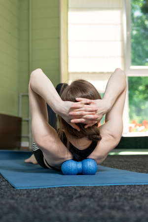 Girl lies on yoga mat and does back massage with roller for physiotherapy. Myofascial release with...