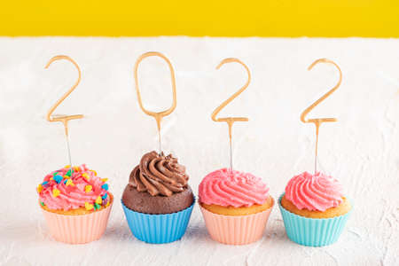 New year cupcakes and gold sparklers numbers 2022. Holiday muffins with pink buttercream frosting on white table.の写真素材