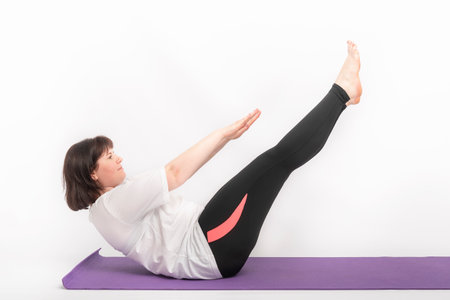 Overweight woman plays sports on yoga mat. Girl rocks the abs. Side view on white backgroundの写真素材