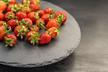 Freshly picked farmers organic strawberries on gray platter. Ripe strawberries with green cuttings