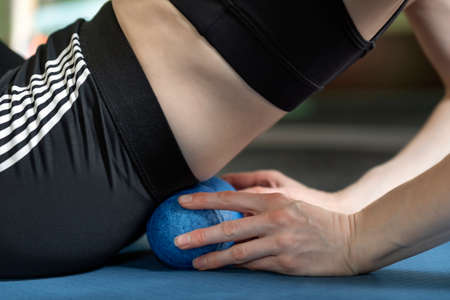 Athletic girl using roller to roll out small of the back muscles. Lumbar massage with ball for MFR. Side view.の写真素材
