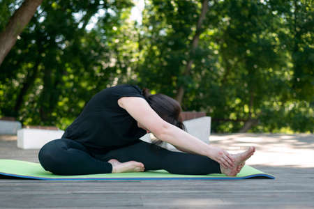 Yoga class in the morning in the park. Side view. Young beautiful flexible girl makes a lean forward...