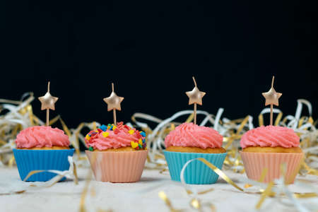 Birthday cupcake with candles in the form of stars in festive tinsel on black background. Space for...