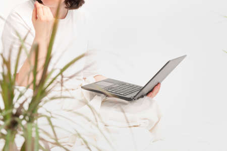 Woman works with laptop sitting on floor near houseplants. Home work.