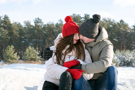 Teenagers sit and hug against the background of the winter forest. Date outdoors.の写真素材