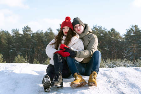 Portrait of young man and woman sit and hug on the snow against the background of the forest and the...