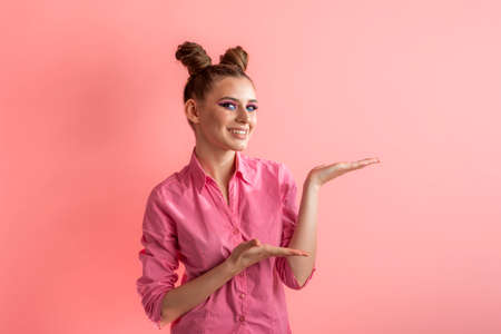 Funny young woman wears rosy shirt and two bun hairstyle. Girl holding something. Blank copy space for text on pink backgroundの写真素材