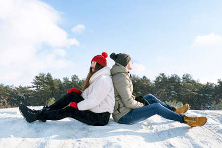 Guy and girl sit back to back in the snow. Active winter recreation.の写真素材