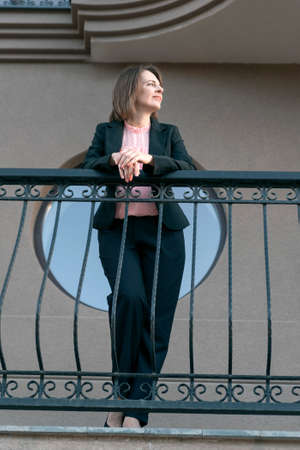 Female chief in black pantsuit on the balcony. Middle-aged woman in formal business clothingの写真素材