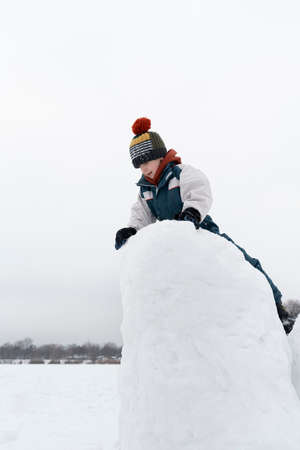 Child sculpts snow castle. Boy builds fortress out of snow. Winter holidays. Vertical frame