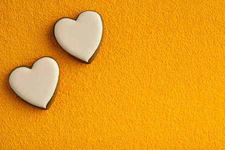 Two white heart shaped cookies with sugar icing on yellow background. Space for textの写真素材
