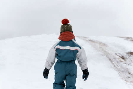 Back view the child walks in the winter on the street. Boy walks on loose snow. Cold winter dayの写真素材