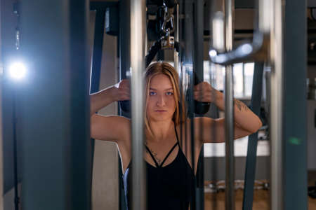 Portrait of a girl in the gym. Young woman trains triceps muscles at the Cable Machine