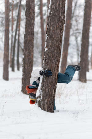 Boy walks in the park and hides behind a tree. Child has fun in the winter park. vertical frame.の写真素材