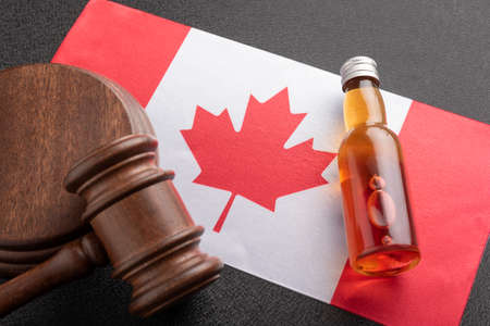 Alcohol and crime concept. Bottle of alcohol and wooden gavel as symbol of law and flag of Canada.の写真素材