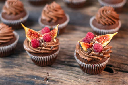 Delicious chocolate muffins with butter cream, raspberries and fig pieces. Coffee cupcakes on wooden table, close-up.の写真素材